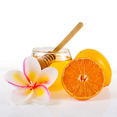 Honey with orange, lemon, candle in the shape of frangipani flower and halved orange isolated on a white background.