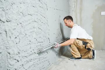Plasterer using screeder smoothing putty plaster mortar on wall