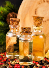 Bottles of oil with wooden stump (cut log), different peppercorns and fir branches.