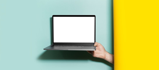 Close-up of male hand holding laptop with mockup between two studio backgrounds of yellow and aqua menthe colors.
