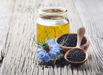 Black cumin oil with flower nigella sativa on wooden table