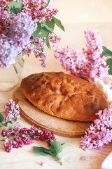 Homemade Apple pie on a wooden table next to a bowl of lilacs. Gentle toning.