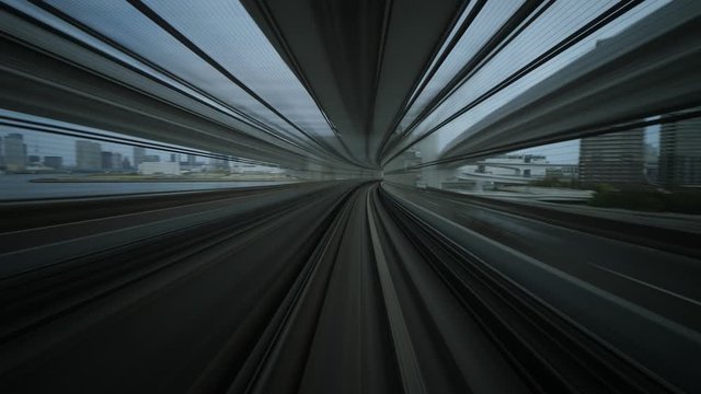 Modern mass transit system at Japan, view back from cabin to elevated track, vehicle make turn and pass first deck of bridge, looks like tunnel due to motion blur