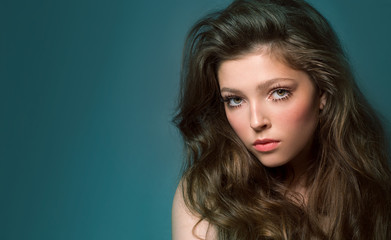 Fototapeta premium A beautiful young woman with long dark hair and long false eyelashes in bunches on a blue background is looking directly at the camera. The beauty.,