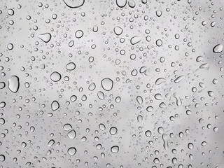 Many big raindrops on a transparent glass against a cloudy blue sky. Condensation and precipitation concept.