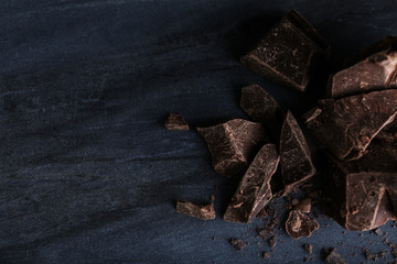 Pieces of dark chocolate on blue marble table, flat lay. Space for text