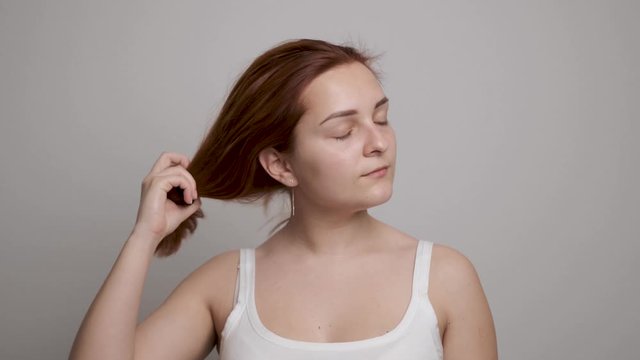 Girl taking off rubber band from red hair after a long daily routine. Grey background
