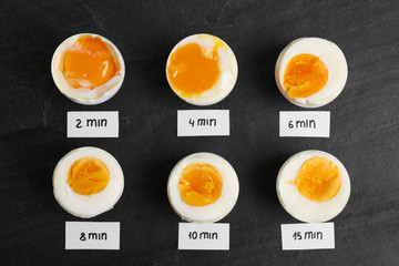 Different cooking time and readiness stages of boiled chicken eggs on black table, flat lay