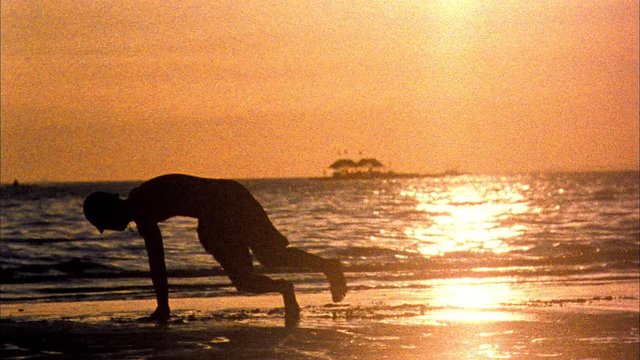 Old archival footage of a breakdancer dancing on a beach in the Philippines as sun sets behind him, film burn, scratches, grain and scratches captured on Super 8 film