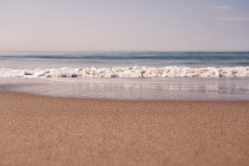 Blurred sea wave with foam on a sandy beach with horizont as a natural background/texture.