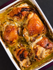 Baked chicken thighs with onions in ceramic form on a stone table, copy space.