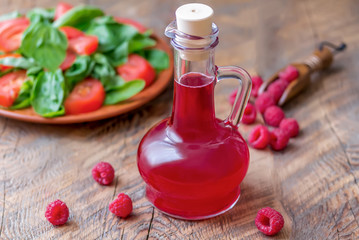 Raspberry vinegar/vinaigrette salad dressing in glass cruet on a wooden background with plate of...