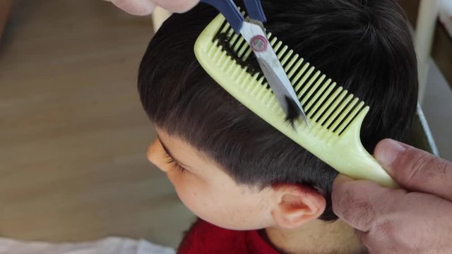 Hair cutting at home. Epidemic of coronavirus infection COVID-19. Hairdressers are closed.A serious child on a haircut by dad. A boy in red clothes is scissored by cutting bangs on his head.