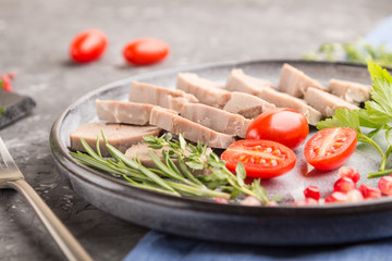 Boiled pork tongue with tomatoes and herbs on a black concrete background. side view, selective focus.