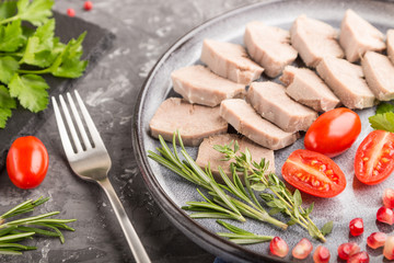 Boiled pork tongue with tomatoes and herbs on a black concrete background. side view, selective focus.