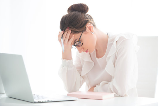 An Upset Young Woman Is Sitting In An Office At A Laptop, And Is Holding Her Head In Her Hands. Problems At Work