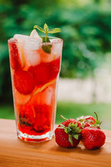 Fresh cold lemonade with strawberries and lemon on wooden background. Citric, healthy