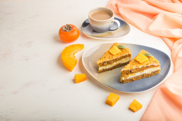 Homemade cake with persimmon and pumpkin and a cup of coffee on a white wooden background with orange textile. side view, copy space.