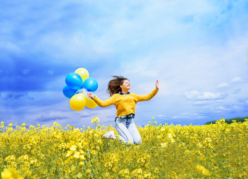 Jumping teenager girl in a field with airy blue and yellow balloons. A blue sky and a yellow field with blooming rapeseed.The concept of freedom and celebration. Girl's birthday