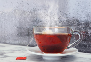 Cup of hot tea near window on rainy day