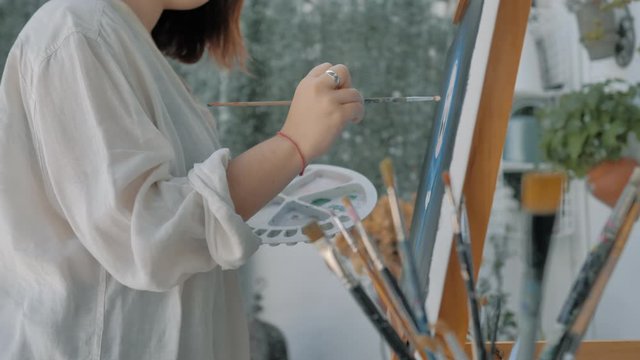 plano lateral de ni&ntilde;a joven con bata blanca pintando obra de arte en exterior