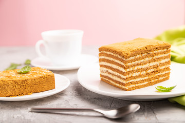 Homemade honey cake with milk cream and mint with cup of coffee on a and pink background. Side view, close up.
