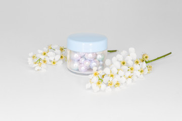 Elegant blue plastic cosmetic jar with pearls and with cherry blossoms on white background. Side view 