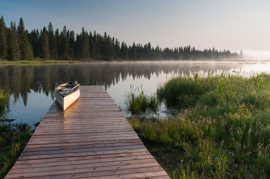 Canoe on a dock at a lake during a misty sunrise.