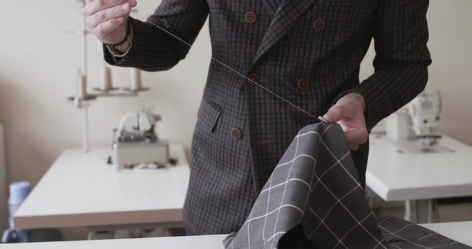 View of tailor's hands stitching a fabric curve on a desktop
