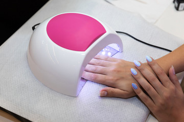 Close-up beautiful woman hands and lamp for nails on table. Nail gel salon. UV lamp. Process of drying gel on nails. Beauty and self care. Modern technology in nail salon. Nail care after quarantine