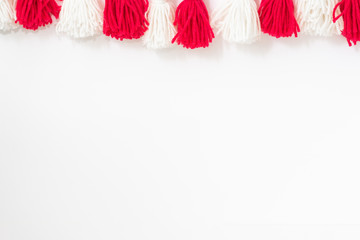 brushes from yarn of red and white color on a white background. Space for copy space. DIY yarn brushes. Garland. Garland of yarn. Pampushki from yarn. Children's creativity