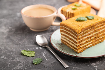 Homemade honey cake with milk cream and mint with cup of coffee on a black concrete background. Side view, selective focus.
