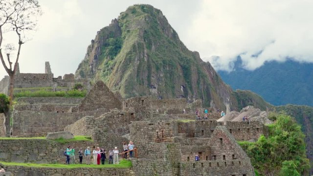 Slow motion tilt up of tourists exploring famous old ruins against mountain peak - Machu Picchu, Peru