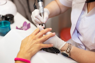 Close-up hardware manicure in salon. Removal of old gel varnish. Manicure master doing beauty procedure for client. Nail care after quarantine. Female hands of a manicurist in white gloves