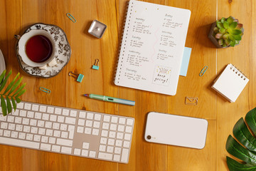 Flat lay of cozy workplace. Schedule planner, keyboard, phone and tea on wooden background.