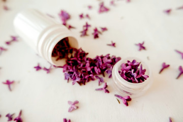 Obraz na płótnie Canvas White jar with lilac petals on a white background, facial massager, alternative medicine and skin care.