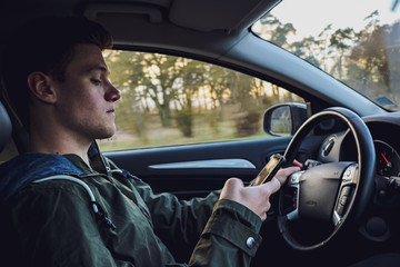 young white man driving a modern car with focusing on his smartphone