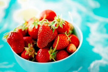 red juicy ripe strawberries in a blue vase on a light background on a blue stand made of epoxy resin. Healthy spring breakfast, fruit plate.