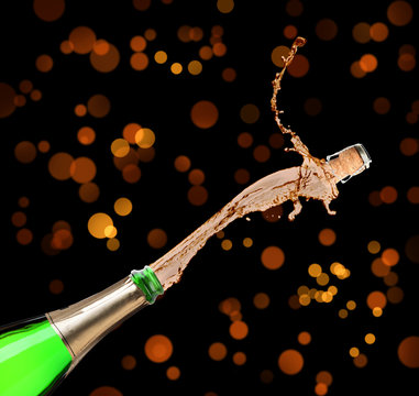 Champagne splashing out of bottle on color background