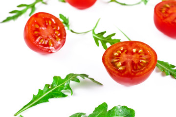 Halved red cherry tomatoes with green rucola leaves isolated on a white background.