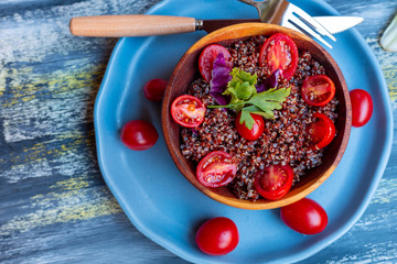 Red quinoa salad with tomato on a rustic table. Superfood and healthy eating concept.