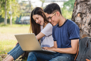 Young man and girls friend classmates sitting at park under tree