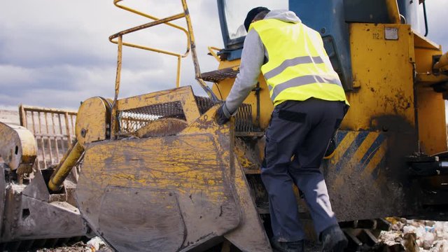 Worker getting in waste excavator on landfill, environmental concept.