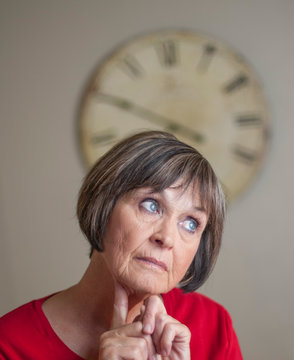 Woman reacts with doubt and unsureness as she contemplates time on the large wall clock behind her.