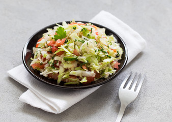 Salad of fresh vegetables cabbage and tomatoes with parsley and green onion on a plate on a linen napkin on a light background