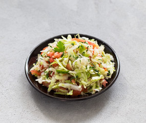 Salad of fresh vegetables cabbage and tomatoes with parsley and green onion on a plate on a light background
