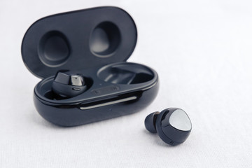 In ear headphones displayed in front of opened black wireless earbud charging case - Front side angled view.