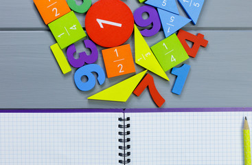 Colorful math fractions, numbers on open notebook and pencils on gray wooden background. Interesting, fun mathematics for kids. Education, back to school concept	
