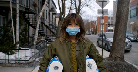 Woman wearing face mask and gloves walks home quickly from supermarket carrying a role of toilet paper which are in short supply during the coronavirus pandemic