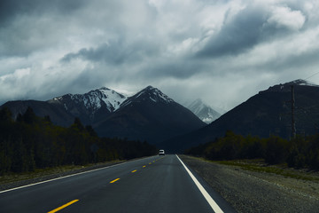 Ruta hacia montañas oscuras con nieve y cielo con nubes.